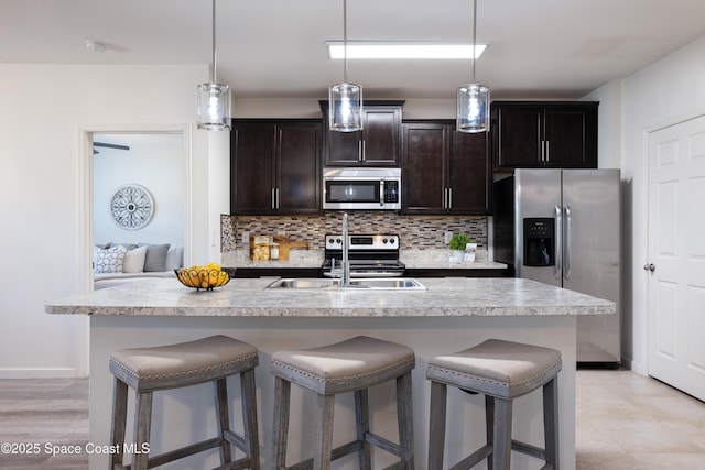 kitchen with pendant lighting, backsplash, stainless steel appliances, and an island with sink