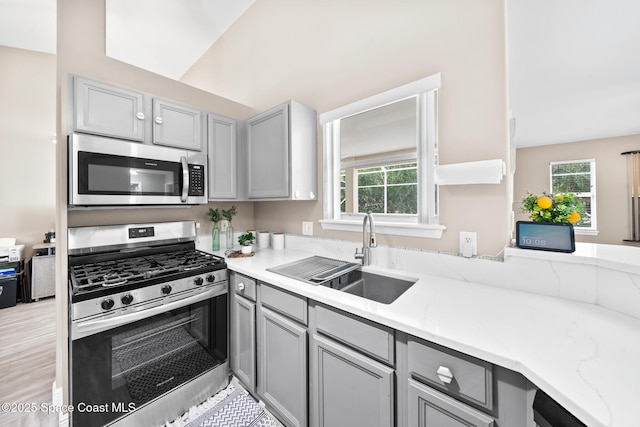 kitchen featuring sink, gray cabinetry, light stone counters, plenty of natural light, and stainless steel appliances