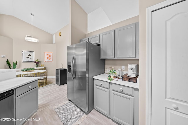 kitchen featuring pendant lighting, lofted ceiling, appliances with stainless steel finishes, gray cabinetry, and light hardwood / wood-style floors