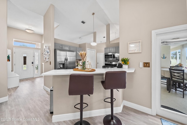 kitchen with light hardwood / wood-style flooring, appliances with stainless steel finishes, a kitchen breakfast bar, gray cabinets, and kitchen peninsula