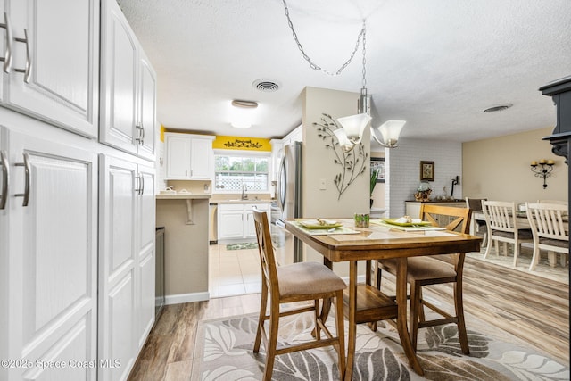 dining room with sink, a textured ceiling, and light hardwood / wood-style floors