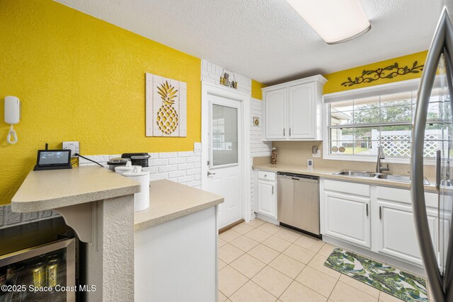 kitchen with sink, light tile patterned floors, dishwasher, white cabinetry, and a textured ceiling