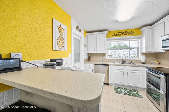 kitchen featuring appliances with stainless steel finishes, sink, white cabinets, light tile patterned floors, and kitchen peninsula