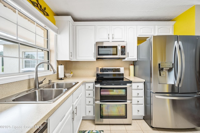 kitchen featuring sink, stainless steel appliances, a textured ceiling, white cabinets, and light tile patterned flooring