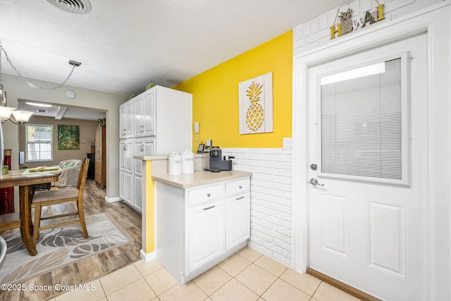 kitchen with white cabinetry, brick wall, a textured ceiling, and light tile patterned floors