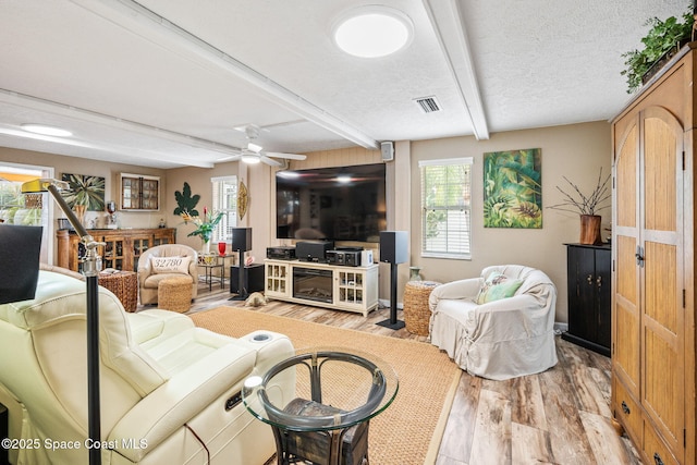 living room featuring beamed ceiling, ceiling fan, light hardwood / wood-style floors, and a textured ceiling