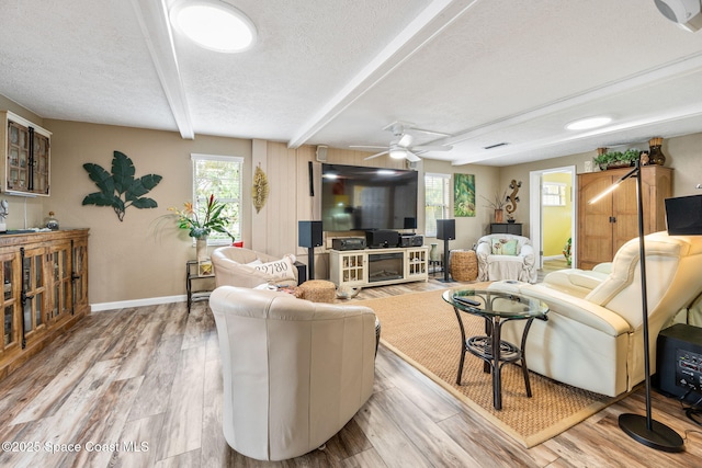 living room with beamed ceiling, ceiling fan, light hardwood / wood-style flooring, and a textured ceiling