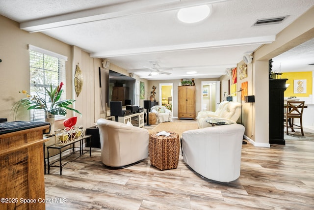 living room featuring beam ceiling, light hardwood / wood-style floors, and a textured ceiling