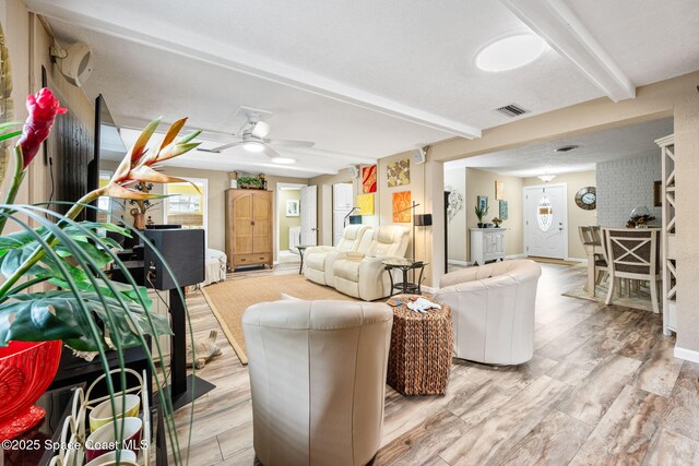 living room featuring ceiling fan, light hardwood / wood-style floors, and beamed ceiling