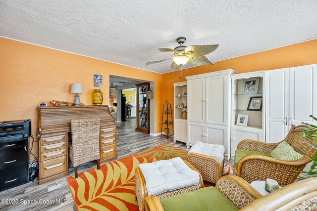 living room with a textured ceiling, ceiling fan, and light hardwood / wood-style flooring