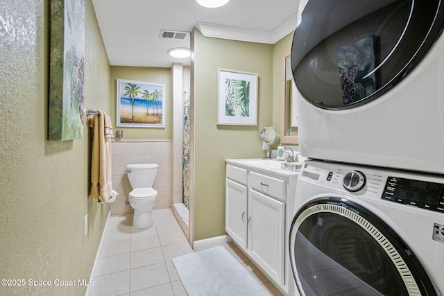 laundry room featuring sink, tile walls, stacked washer and clothes dryer, light tile patterned floors, and crown molding