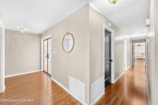 hall with light wood finished floors, visible vents, a textured ceiling, and baseboards