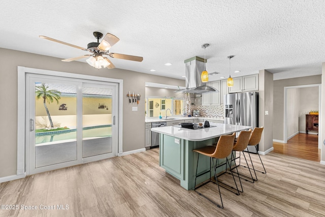 kitchen featuring a center island, stainless steel appliances, island range hood, light countertops, and decorative backsplash