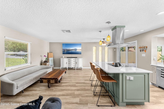 kitchen featuring visible vents, light countertops, green cabinets, black electric cooktop, and island range hood