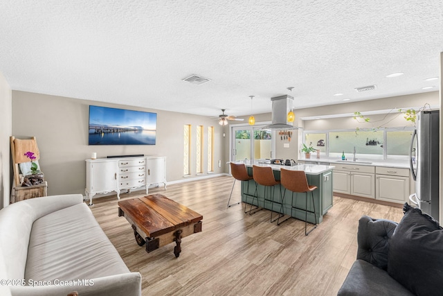 living area featuring visible vents, baseboards, a textured ceiling, and light wood-style flooring