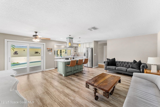 living area with baseboards, visible vents, light wood-style flooring, ceiling fan, and a textured ceiling