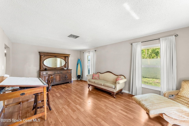 living room with baseboards, light wood-style floors, visible vents, and a textured ceiling