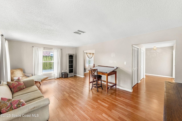 living room featuring a textured ceiling, baseboards, visible vents, and light wood-type flooring