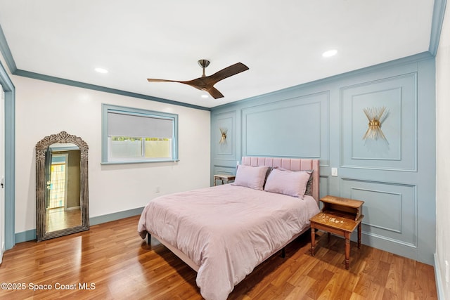 bedroom featuring a ceiling fan, baseboards, ornamental molding, light wood-style floors, and a decorative wall