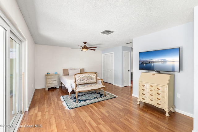 bedroom with baseboards, visible vents, light wood finished floors, and a textured ceiling