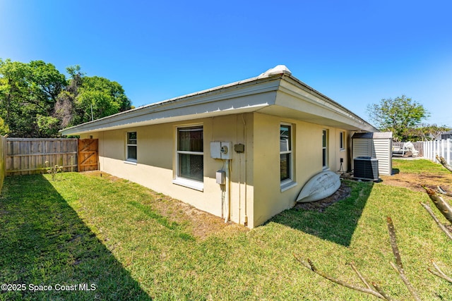 rear view of house featuring a yard, a fenced backyard, central AC, and stucco siding