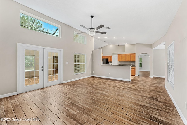 unfurnished living room featuring light hardwood / wood-style flooring, high vaulted ceiling, french doors, and ceiling fan