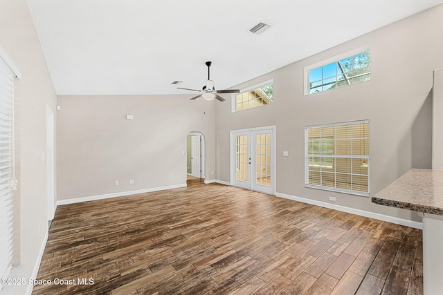 unfurnished living room featuring french doors, ceiling fan, a towering ceiling, and hardwood / wood-style flooring