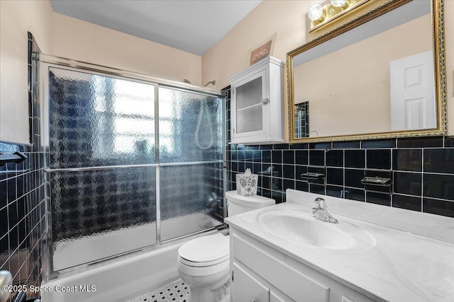 full bathroom featuring toilet, vanity, bath / shower combo with glass door, and tile walls