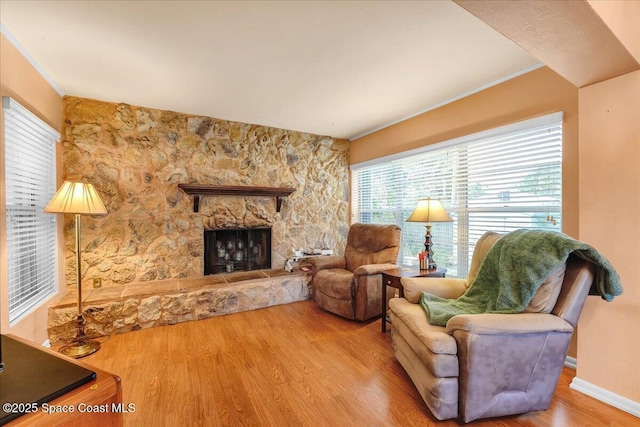 living room featuring hardwood / wood-style floors, a stone fireplace, and ornamental molding