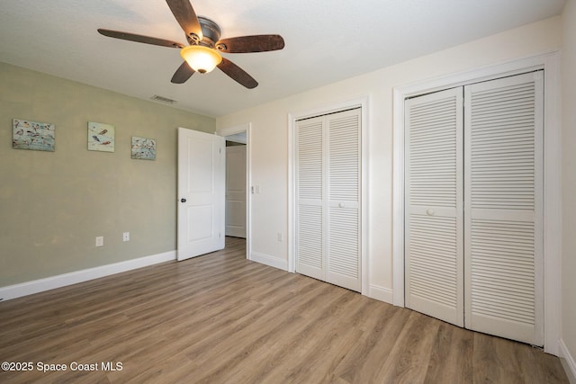 unfurnished bedroom featuring multiple closets, visible vents, light wood-style floors, ceiling fan, and baseboards