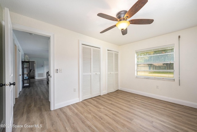 unfurnished bedroom featuring visible vents, light wood-style flooring, baseboards, and two closets