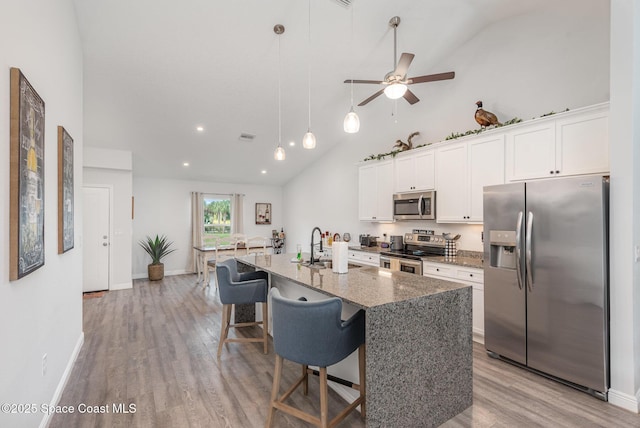 kitchen with dark stone countertops, stainless steel appliances, a center island with sink, and white cabinets