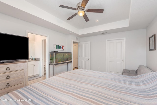 bedroom featuring connected bathroom, ceiling fan, and a tray ceiling