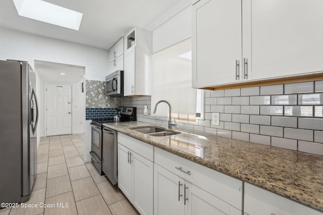 kitchen with appliances with stainless steel finishes, white cabinetry, sink, backsplash, and light stone counters