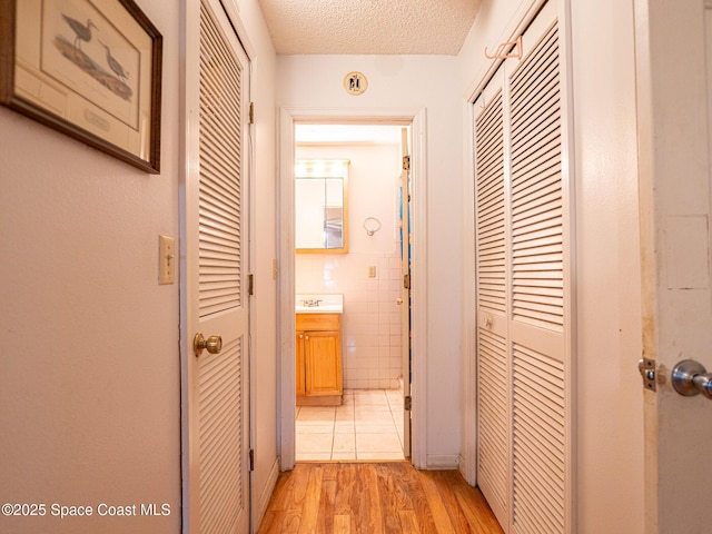 corridor with tile walls, sink, a textured ceiling, and light wood-type flooring