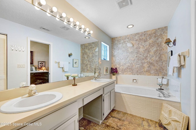 bathroom featuring a relaxing tiled tub, vanity, and a textured ceiling