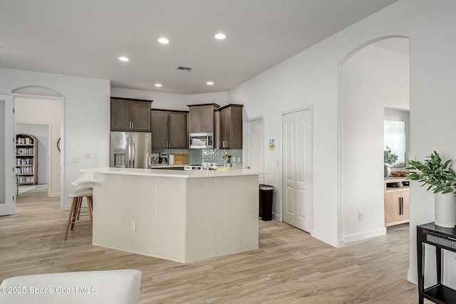 kitchen with dark brown cabinets, appliances with stainless steel finishes, light hardwood / wood-style floors, and a kitchen island