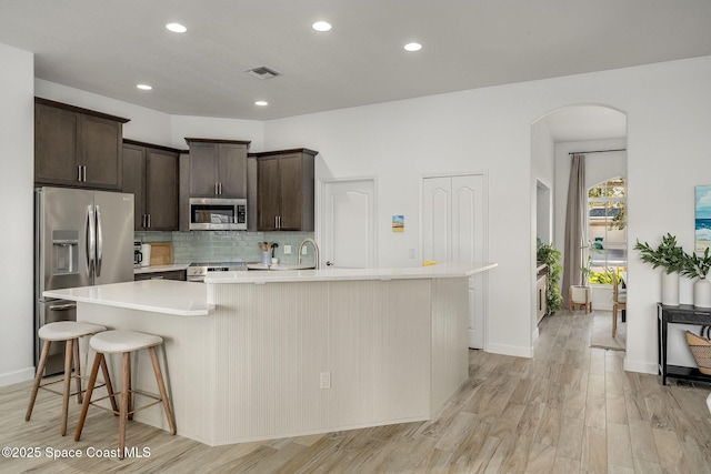 kitchen featuring appliances with stainless steel finishes, a breakfast bar, backsplash, a kitchen island with sink, and dark brown cabinets