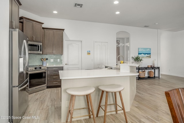 kitchen featuring light hardwood / wood-style flooring, stainless steel appliances, an island with sink, and a breakfast bar