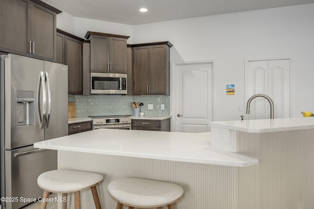 kitchen with sink, dark brown cabinets, stainless steel appliances, a kitchen breakfast bar, and tasteful backsplash