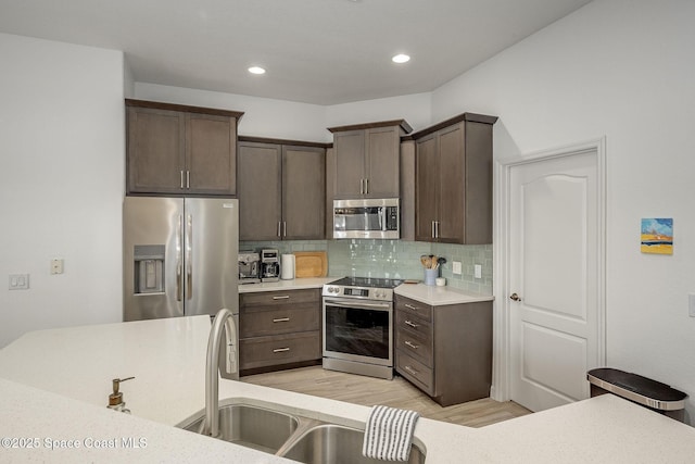 kitchen featuring sink, appliances with stainless steel finishes, dark brown cabinets, light hardwood / wood-style floors, and decorative backsplash