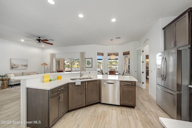 kitchen with appliances with stainless steel finishes, sink, light wood-type flooring, and decorative light fixtures