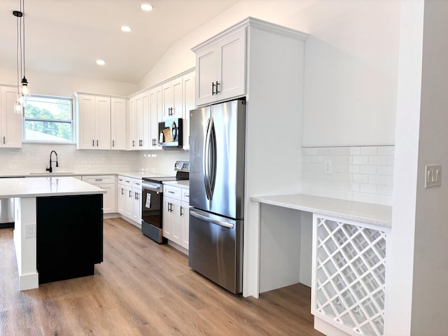 kitchen with appliances with stainless steel finishes, decorative light fixtures, white cabinetry, sink, and light hardwood / wood-style flooring