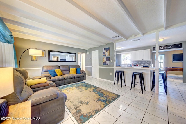 living room featuring light tile patterned flooring, a textured ceiling, and beamed ceiling