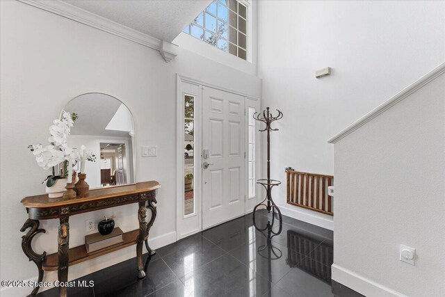 foyer featuring ornamental molding, granite finish floor, a high ceiling, and baseboards