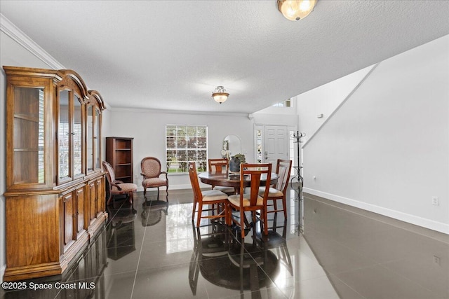 dining room featuring crown molding, baseboards, a textured ceiling, and dark tile patterned flooring