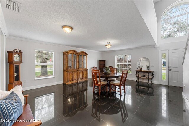 dining room with a textured ceiling, ornamental molding, visible vents, and baseboards