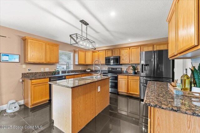 kitchen featuring an island with sink, appliances with stainless steel finishes, dark tile patterned flooring, and decorative light fixtures