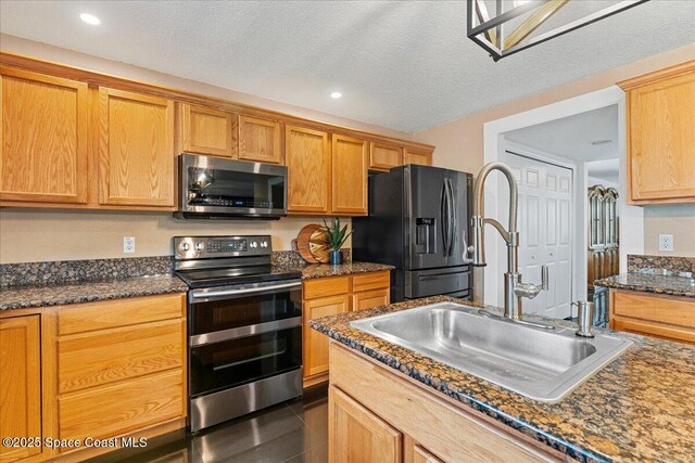 kitchen featuring a textured ceiling, dark tile patterned floors, a sink, appliances with stainless steel finishes, and dark stone countertops