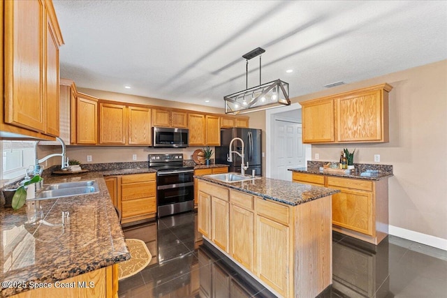 kitchen featuring appliances with stainless steel finishes, decorative light fixtures, a center island with sink, and a sink